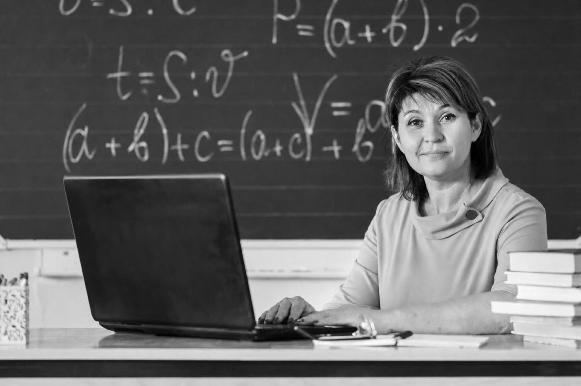 A teacher reviewing a class progress dashboard on a laptop at a classroom desk