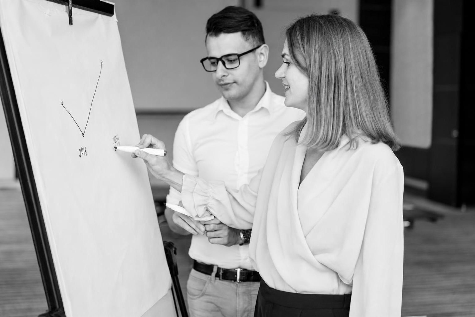 Two people at a whiteboard crossing out a list of planned features