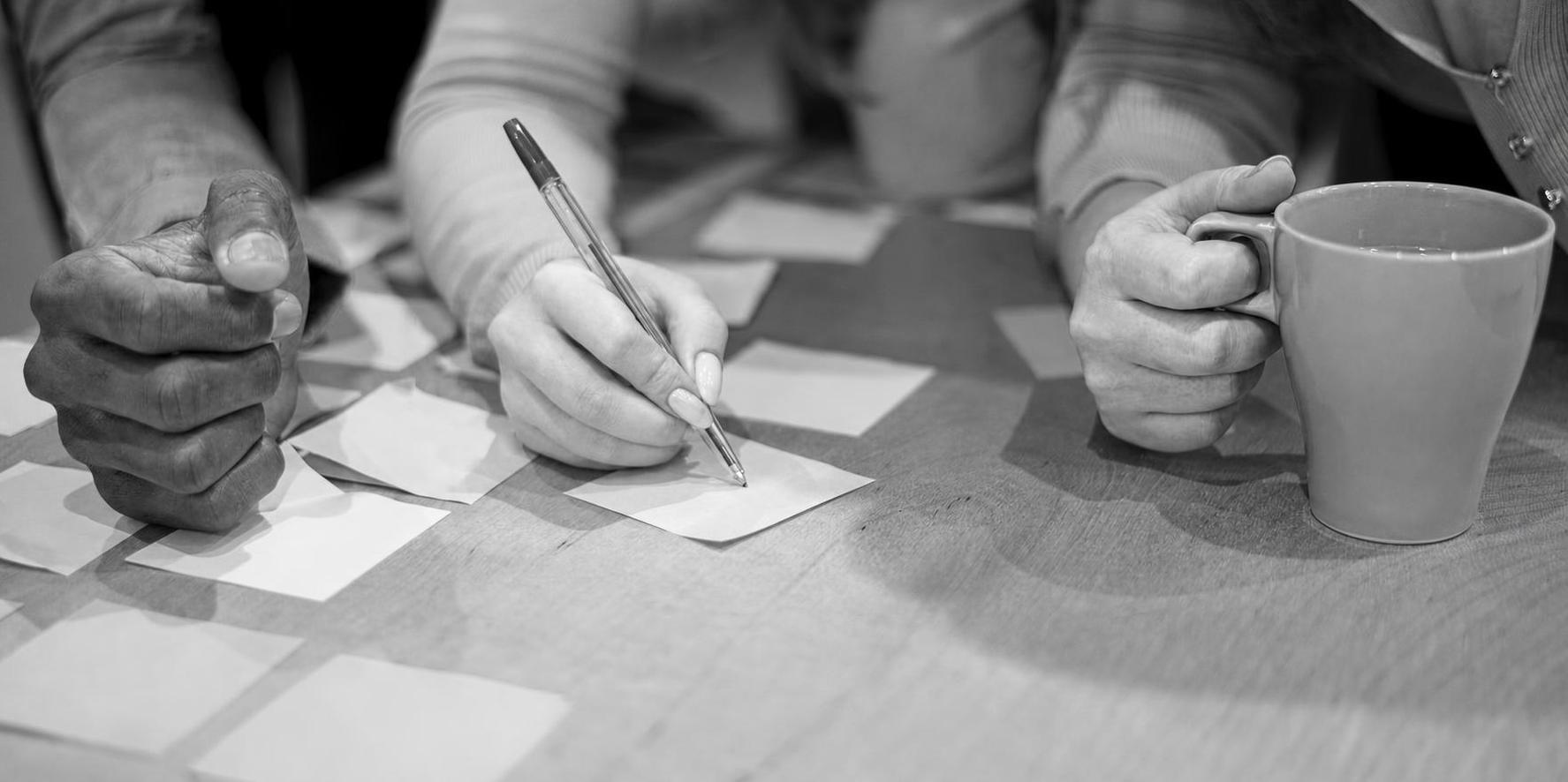 Hands writing priorities on sticky notes around a cup of coffee